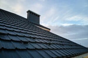 Ein schwarzes Dach in der Dachsanierung Apolda mit Kamin und Himmel.